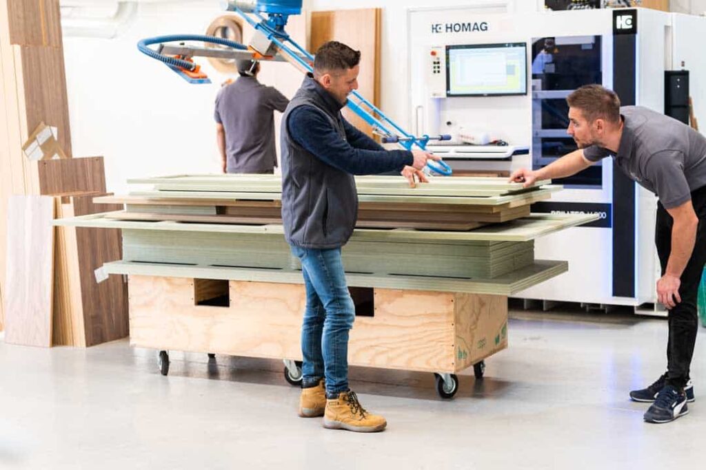 Two craftsmen carefully measuring and discussing a large piece of wood for a wardrobe