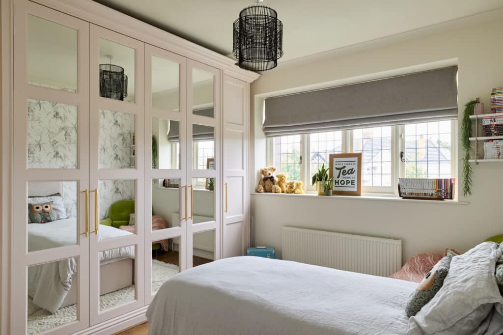 Pink fitted wardrobes with sectioned mirrored doors in a bedroom setting