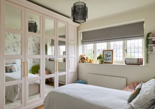 Pink fitted wardrobes with sectioned mirrored doors in a bedroom setting
