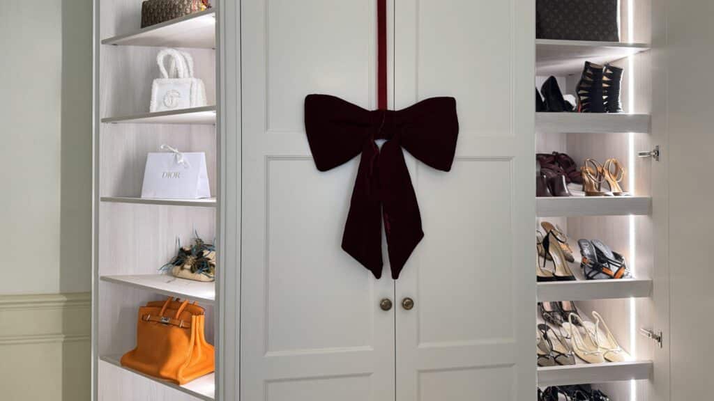 White open-fronted walk in wardrobe with Christmas bow hanging on closed wardrobe doors