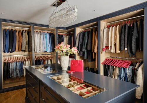 Open fronted bespoke walk-in wardrobe with glass-topped island and internal lighting
